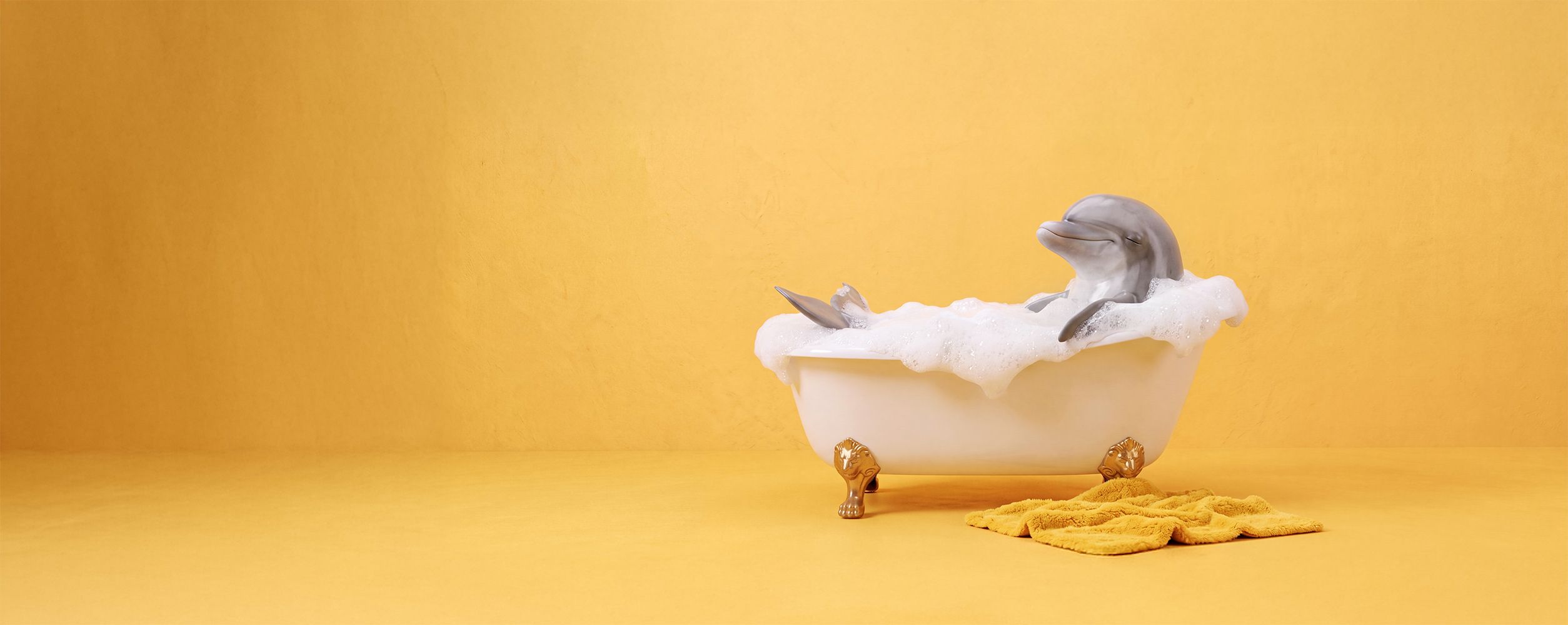 Delfi der Delfin entspannt in einer schaumgefüllten Badewanne vor einem gelben Hintergrund